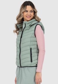 Gilet imbottito verde chiaro con cappuccio, dotato di zip frontale, due tasche laterali e rifiniture nere. Indossato sopra una maglietta a maniche lunghe rosa.