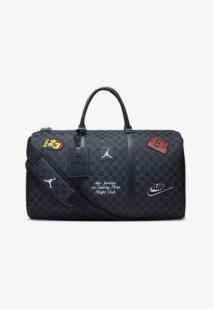 Černá sportovní taška s potištěnou textilií, dvojitými horními uchy, nastavitelným ramenním popruhem a barevnými nášivkami a logy.