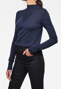 Jersey de color azul marino con cuello alto tipo mock y diseño ajustado. Presenta un patrón triangular texturizado en el pecho y puños acanalados.