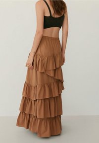 Jupe maxi brune à plusieurs niveaux avec de nombreux volants. Fabriquée en tissu doux, elle présente une taille élastique et arrive jusqu'à la cheville.