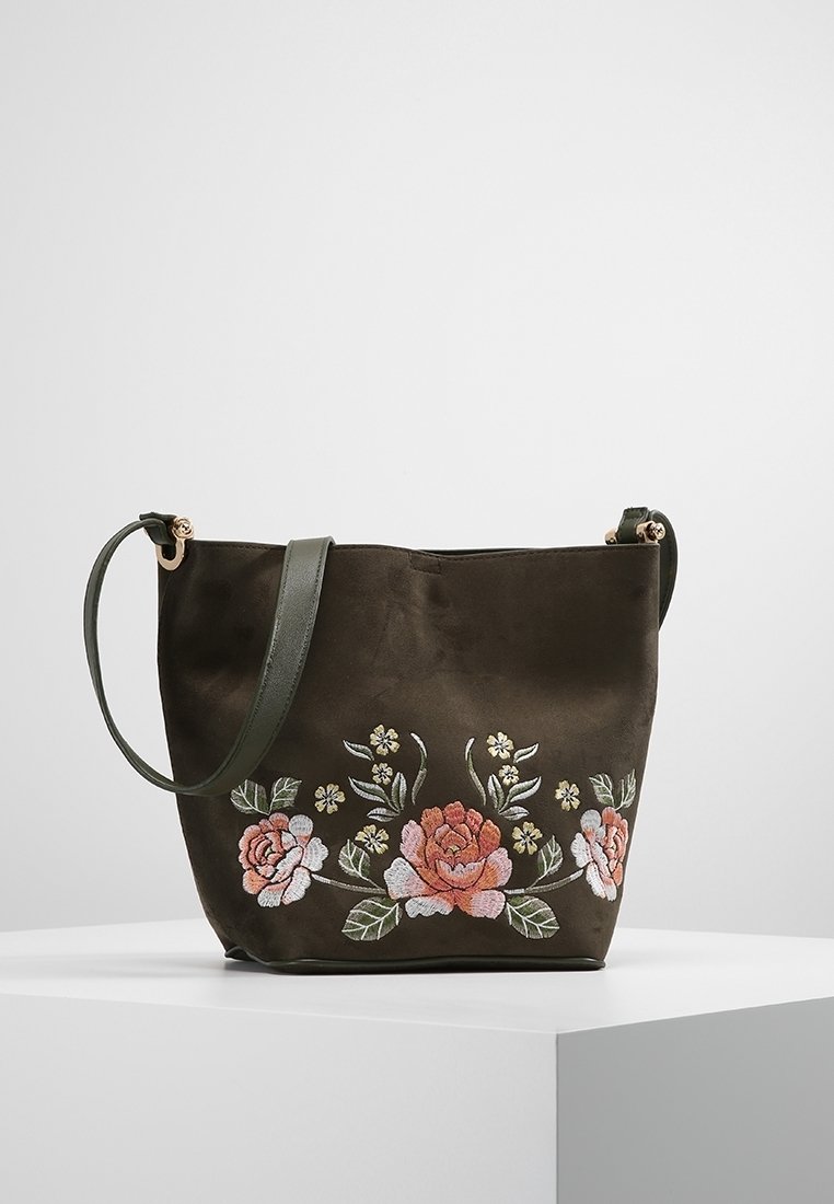 Sac fourre-tout en tissu vert olive avec broderie florale en rose, blanc et vert. Dispose d'une longue bandoulière ajustable et de quincaillerie en or rose.