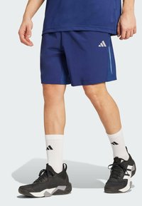 Bermudas deportivas de color navy con acentos laterales, tela ligera, combinadas con zapatillas negras y calcetines blancos de canalé con franjas negras.