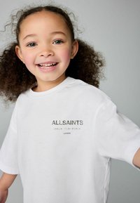 Bijela majica kratkih rukava s izvezenim „ALLSAINTS“ logotipom u tamnosivoj boji i tekstom na dodatnim jezicima. Mekani, glatki pamučni materijal.