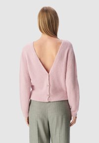Jasnoróżowy, puszysty sweter z głębokim dekoltem z tyłu i zapięciem na guziki. Dłuższe rękawy, dopasowana talia i miękka faktura. W zestawie z spodniami w prążki.