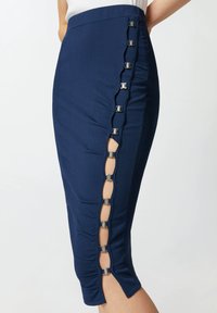 Tamnoplava olovka suknja s rebrastom teksturom, bočnim prorezom s metalnim detaljima i valovitim rubom duž zatvaranja.