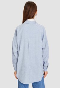 Lyseblå oversized skjorte i blødt stof med knappet krave, lange ærmer, plisseeffekt bagpå og buet kant.