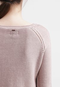 Maglione a maglia di un rosa chiaro con finitura testurizzata, caratterizzato da un collo rotondo e cuciture decorative alle cuciture delle spalle.