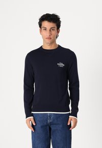 Kék, crew neck pulóver pamutból, fehér bordázott mandzsettákkal és aljjal, kisebb logóval a mellkason és sima felülettel.