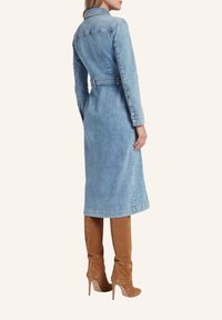 Niebieska sukienka midi z denimu, z kołnierzykiem, długimi rękawami, paskiem w talii oraz prostym krojem, zestawiona z brązowymi botkami do uda.
