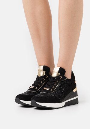 Zapatillas de ante negras con acentos dorados, que presentan adornos brillantes y una suela cuña. Punta redondeada y diseño con cordones.