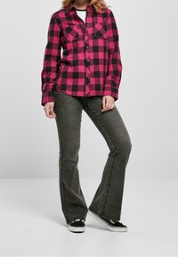 Rosa och svart rutigt skjorta med knappar och långa ärmar samt två bröstfickor, matchad med grå utsvängda jeans och svarta sneakers.