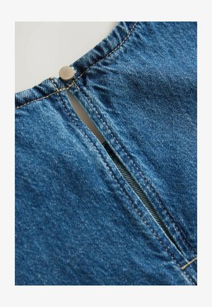 Modra denim tkanina z gumbom, z zasnovo razporke na hrbtni strani. Očitno šivanje in gladka tekstura.