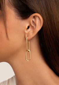 Goudkleurige metalen oorbellen met een paperclip ontwerp, bestaande uit een lange en korte schakel, met een gestructureerde afwerking, hangend aan een eenvoudige studpost.