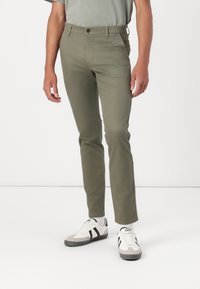 Pantalons fuselés vert olive avec une texture lisse, fermeture à bouton et poches latérales, associés à des baskets blanches avec des accents noirs.
