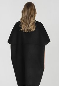 Czarny wełniany ponczo o luźnym kroju, oversize'owej sylwetce i krótkich rękawach; gładka faktura z przeszyciem na plecach.