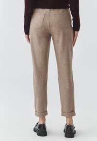 Béžové nohavice z vlnenej zmesi s rolenými manžetami, dvoma zadnými vreckami, slim fit a hladkou textúrou. Čierne topánky dopĺňajú outfit.