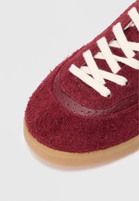 Røde semskede sneakers med en tekstureret finish, der har hvide snørebånd, en glat læderdetalje og en gummisål.