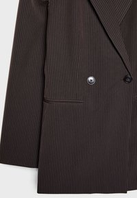 Bruine pinstripe blazer gemaakt van gestructureerde stof, met een scherpe revers, twee knopen en een enkele zak aan de linkerkant.