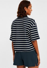 Sininen ja valkoinen raidallinen lyhythihainen paita, jossa on rento istuvuus ja ribbikuvio, yhdistettynä tummiin shortseihin, joiden sivuilla on halkiot.