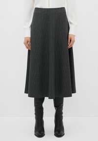 Gonna grigio scuro, lunga fino al ginocchio, con righe bianche verticali, vita aderente e design svasato. Indossata con stivali neri fino al ginocchio.