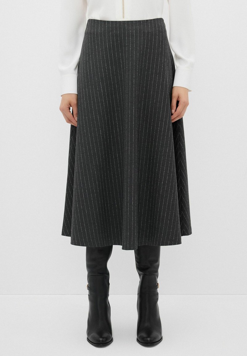 Gonna grigio scuro, lunga fino al ginocchio, con righe bianche verticali, vita aderente e design svasato. Indossata con stivali neri fino al ginocchio.