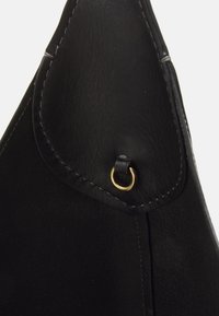 Esquina de bolso de cuero negro con costuras visibles y pequeño detalle de anillo metálico dorado unido por una tira de cuero.