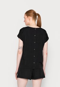 Blusa preta de mangas curtas com decote redondo e fecho de botão nas costas, feita de um tecido suave e com um corte solto.