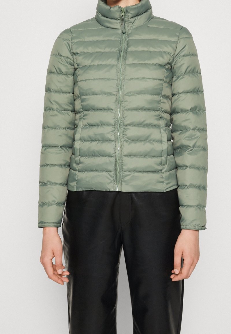 Jasnozielona kurtka puchowa z wysokim kołnierzem, pionowym wzorem pikowania, zamkiem błyskawicznym z przodu i dopasowanymi rękawami.