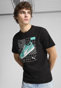 Sort t-shirt med en grafik af turkise sneakers med hvide detaljer og en baggrund med rutemønster. Lavet af glat stof.
