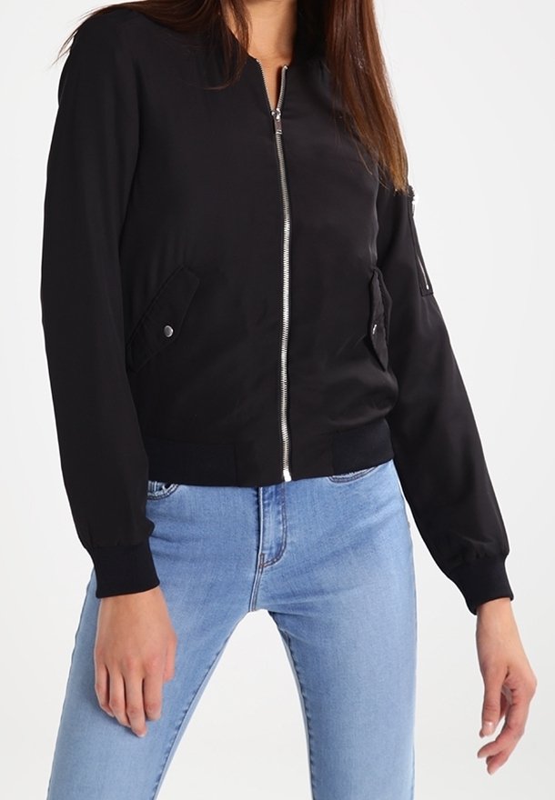 Black bomber jacket with a front zipper, two side pockets, ribbed cuffs, and waistband, made from smooth fabric. Paired with light blue jeans.