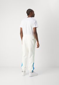 Hvide sweatpants med grønne og blå sidepaneler, elastisk talje og detalje med baglomme; parret med en ensfarvet hvid t-shirt.
