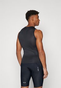 Schwarzes, enganliegendes Sporttanktop aus strukturiertem Stoff, kombiniert mit schwarzen Radshorts mit weißen Akzenten. Rückansicht des Outfits.