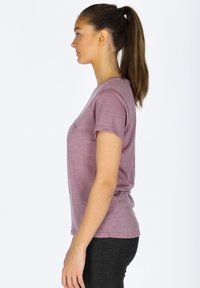 T-shirt a maniche corte e collo rotondo di un leggero malva, realizzato in tessuto morbido con una texture liscia, indossato con leggings neri, mostrato di profilo.