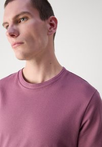 Violet tekstūruotas džemperis su apvaliu iškirpimu, turintis subtilią šešiakampio formos raštą ir trumpomis rankovėmis. Lygi, matinė apdaila.