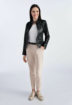 Czarna skórzana kurtka z wysokim kołnierzem i zapinanymi na zamek kieszeniami, w połączeniu z beżowymi spodniami i beżowymi sneakersami. Gładka faktura, dopasowany krój.