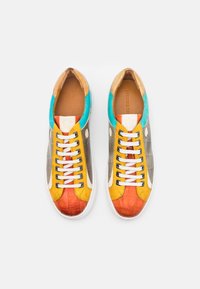 Une paire de baskets basses colorées avec des panneaux orange, jaune, turquoise et gris, des lacets blancs et une semelle blanche sur un fond blanc.