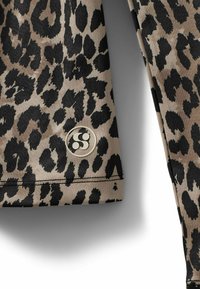 Top de manga larga con estampado de leopardo en beige y negro, con una etiqueta circular con logo. Textura suave con acentos negros contrastantes en las costuras.