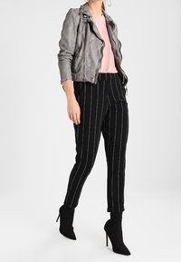 Metalická šedá kožená bunda, růžový top, černé pruhované zúžené kalhoty a černé kotníkové boty s špičatými špičkami doplňují celý outfit.