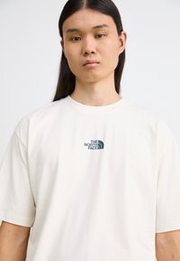 Kremfarget t-skjorte med korte ermer laget av bomull med rund hals. Har en grønn logo av "The North Face" på brystet.