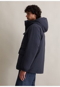 Granatowa kurtka z kapturem, z kieszenią z przodu, elastycznymi mankietami i teksturowaną powierzchnią, charakteryzująca się luźnym krojem i minimalistycznym stylem.