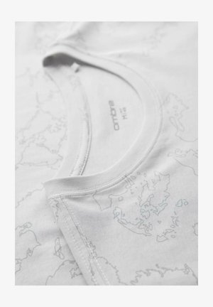 Close-up van de kraag van een wit katoenen T-shirt met een vage grijze kaartprint en een zichtbaar merklint met de tekst "ombre M16".