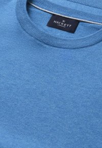 Niebieski sweter dziergany z okrągłym dekoltem, z czarną metką Hackett London przyszytą od wewnątrz kołnierza.