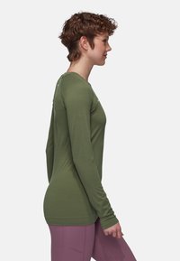 Langärmliges T-Shirt aus olivgrünem Stoff, mit rundem Ausschnitt und taillierter Passform, kombiniert mit enganliegenden, hell-lilanen Leggings.