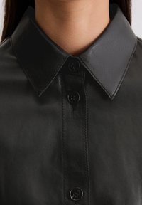 Zbliżenie na osobę noszącą czarną skórzaną koszulę z kołnierzykiem zapiętą pod szyją.