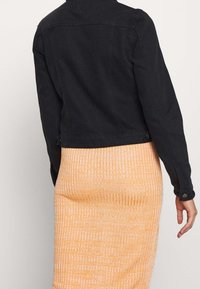 Svart denimjacka med klassisk skärning, knäppte manschetter och en strukturerad design, kombinerad med en orange ribbad stickad kjol.