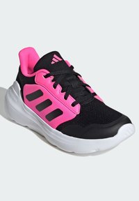 Baskets de sport noires et roses avec une tige en maille, semelle épaisse et trois rayures noires proéminentes sur le côté. Comprend un col rembourré rose.