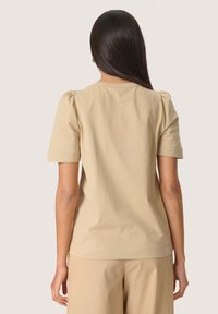 Beige t-shirt med korte ærmer lavet af blødt stof. Har en afslappet pasform med lette puffærmer og en rund halsudskæring.