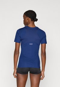 Camiseta deportiva azul marino de manga corta con corte ajustado, con paneles texturizados y un pequeño logo "TECHFIT" en la parte trasera. Se llevan puestos pantalones cortos negros.