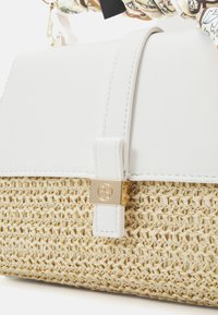 Witte en geweven strohandtas met een gouden sluiting, met een gladde textuur, gestructureerd ontwerp en een decoratieve handgreep met patronen.