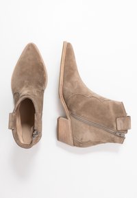 Stivaletti alla caviglia in suede color beige con punta a punta, tacco in legno striato, chiusura con zip laterale e cuciture decorative lungo il davanti.